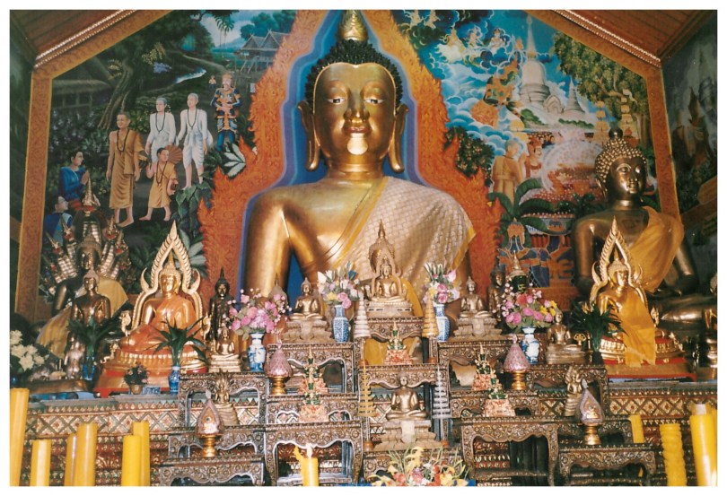 Dozens of small Buddha statues on ornate platforms in front of a large Buddha statue surrounded by a colorful mural