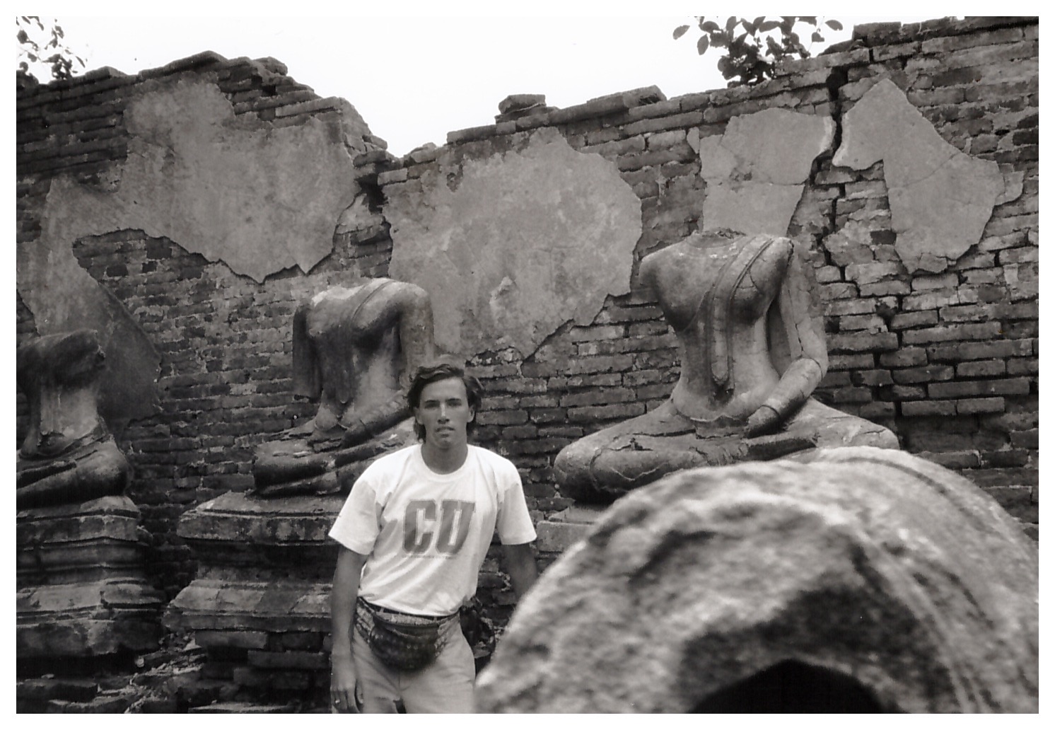 The author standing before three headless Buddha statues in front of a crumbling brick temple wall