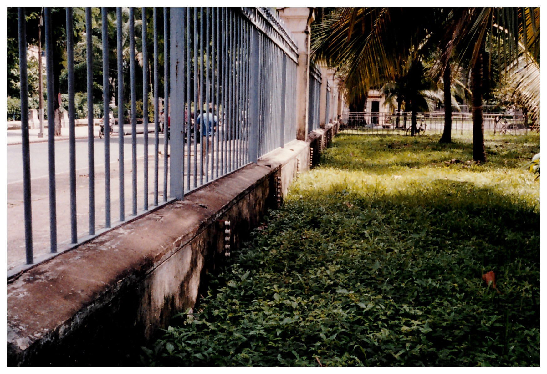Looking down the length of the inside of a tall metal fence set on a short concrete base studded with white ceramic insulators