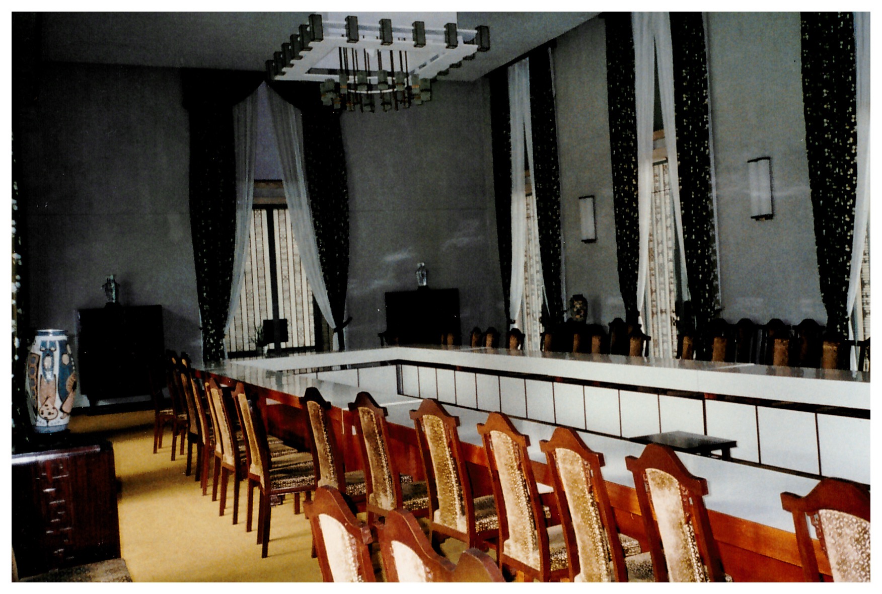 Large conference conference table with at least 15 seats to a side in finely appointed room with 15-foot ceilings and fine furniture and vases
