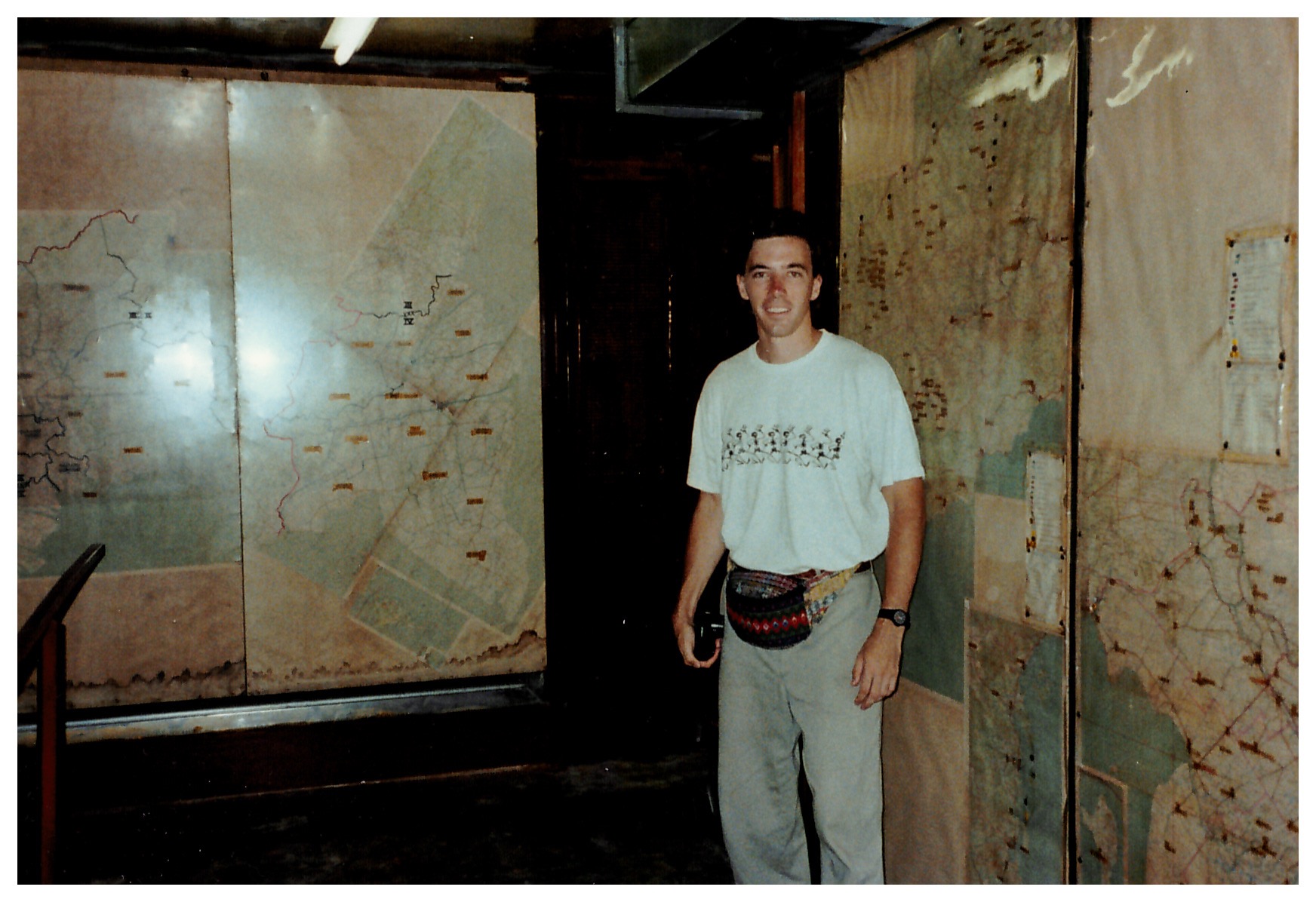 The author standing in a room with old, large, water-stained maps of various regions of Vietnam on the walls