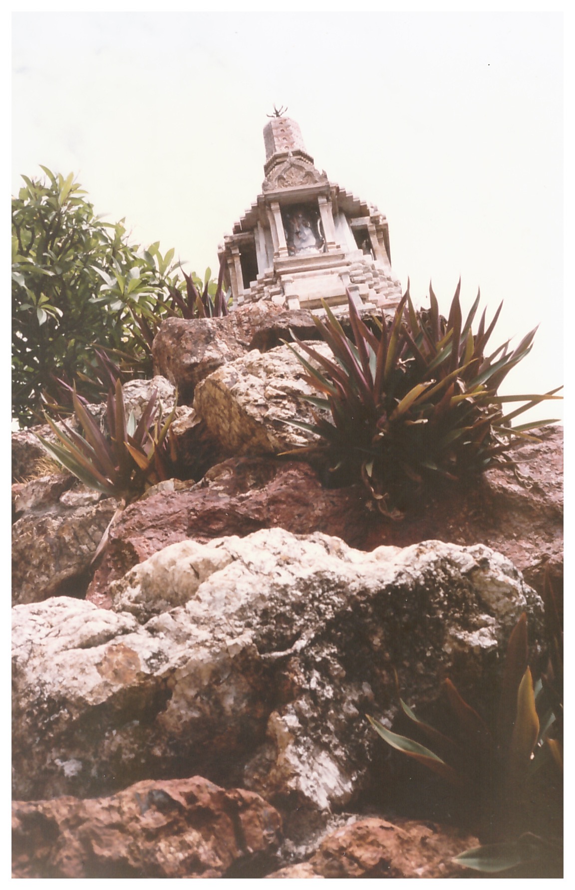 Small shrine seen from below on top of a rocky outcrop with vegetation growing from the rocks
