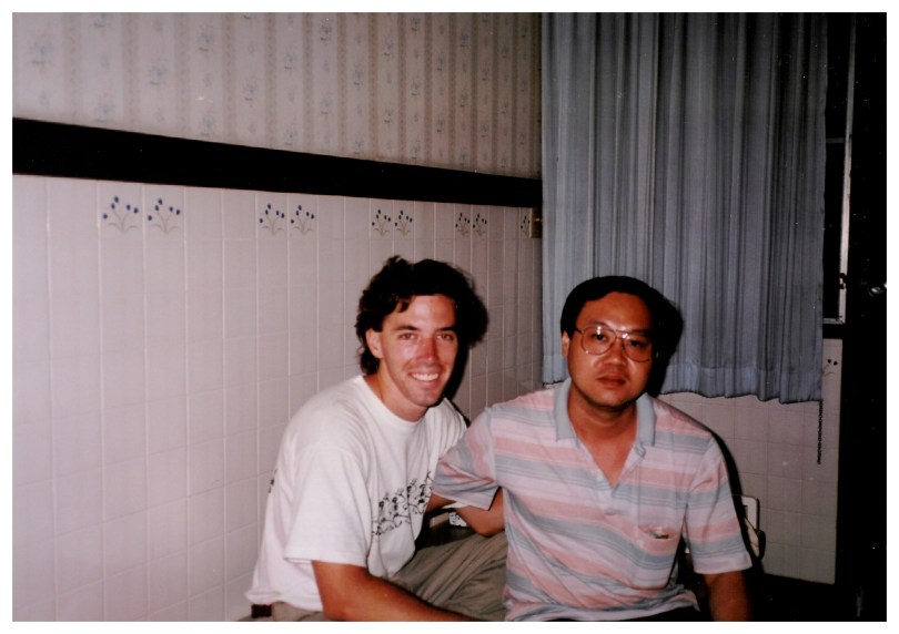 The author with his Thai friend, seated on a day bed in a tile-walled room with blue curtains