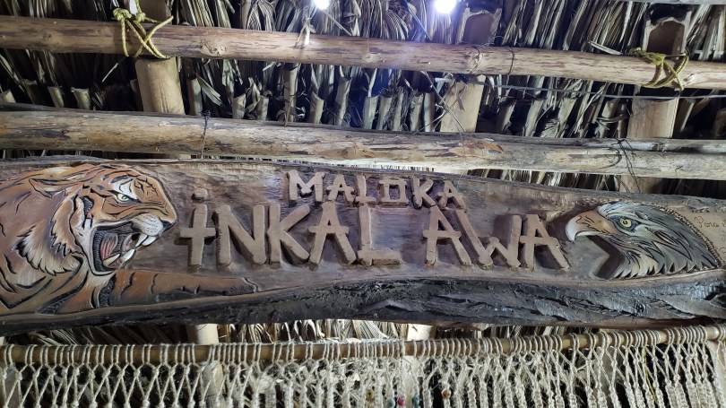 Wooden sign carved with the words Maloka Inkal Awa, flanked by a tiger on the left and eagle or other bird of prey on the right