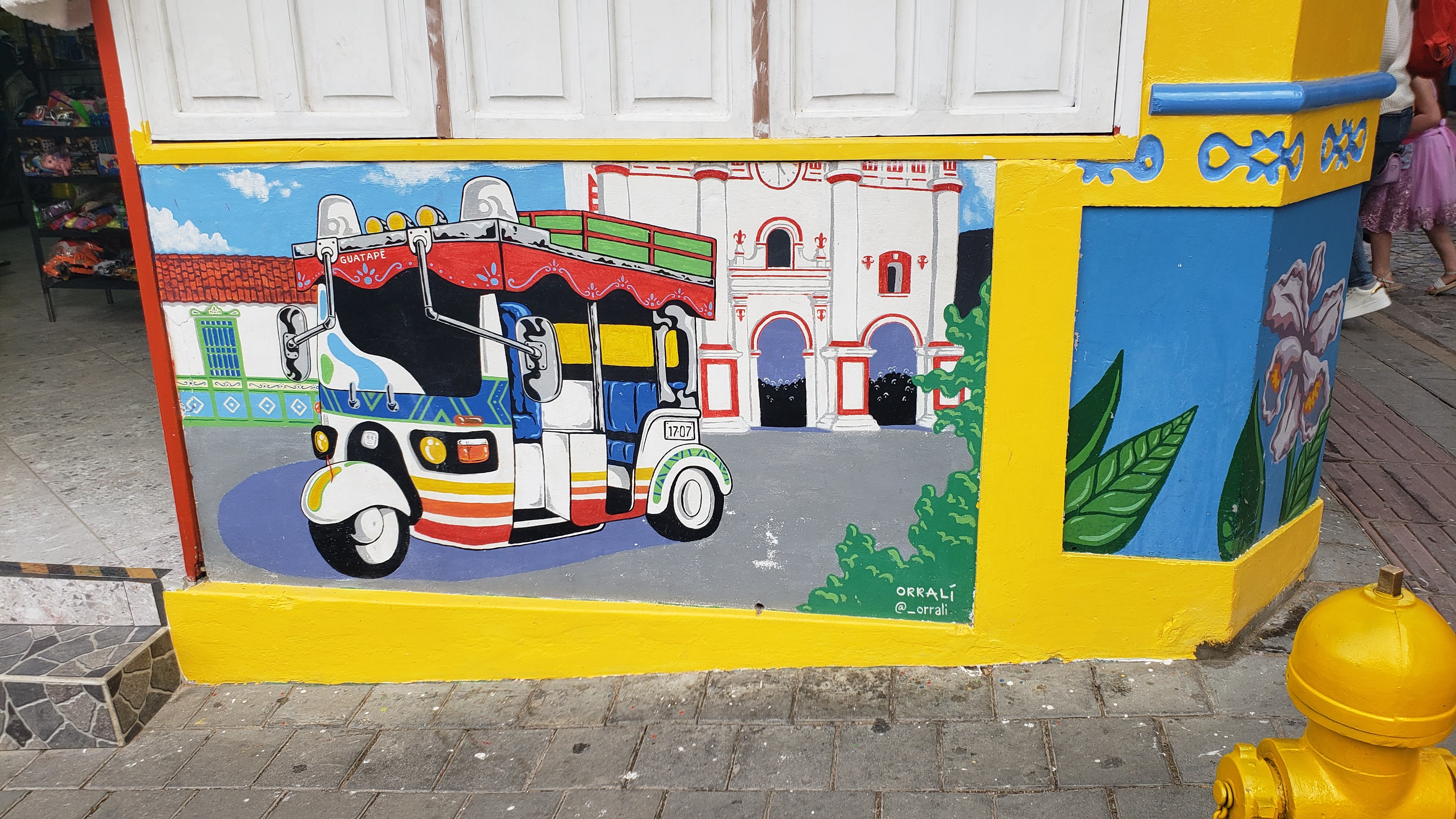 Painting of a colorful tuk tuk on a zócolo with Iglesia de Nuestra Señora del Carmen in the background