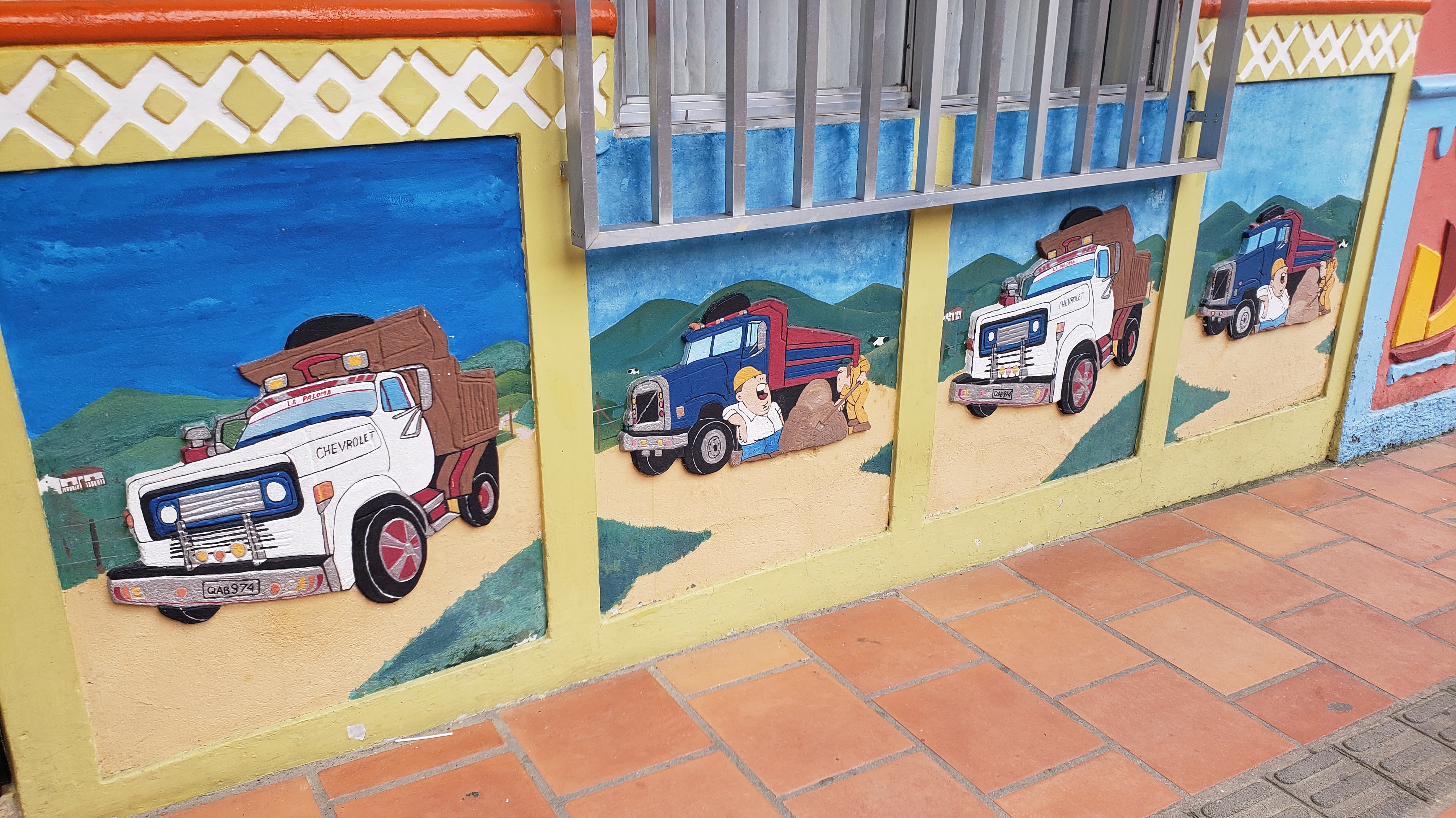 Bas relief of a a white dump truck by itself next to one with a blue dump truck next to a pile of dirt with one man working and one leaning on the truck tire, yawning