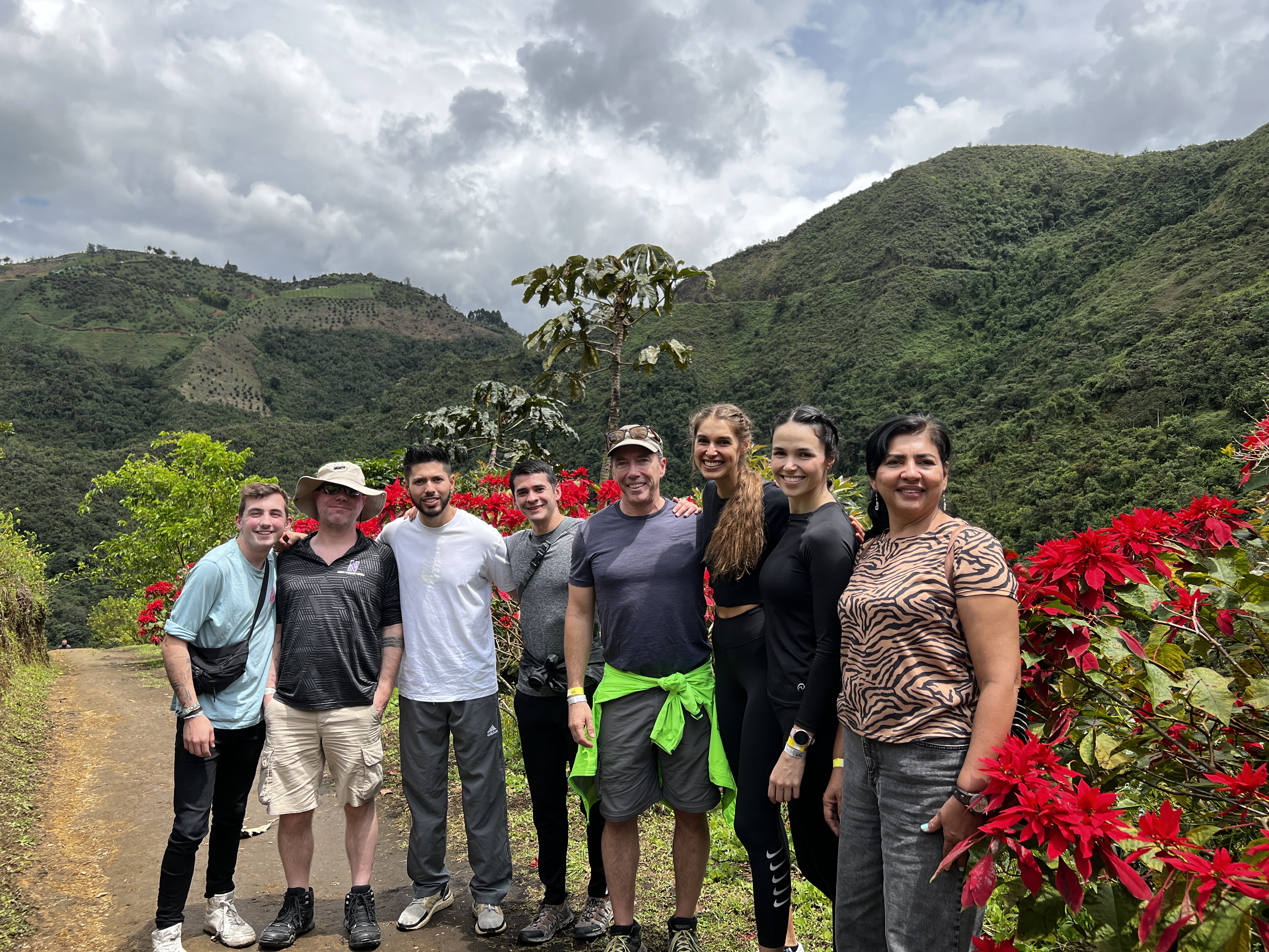 Three women and 5 men posing along a path lined with red flowers among the hills