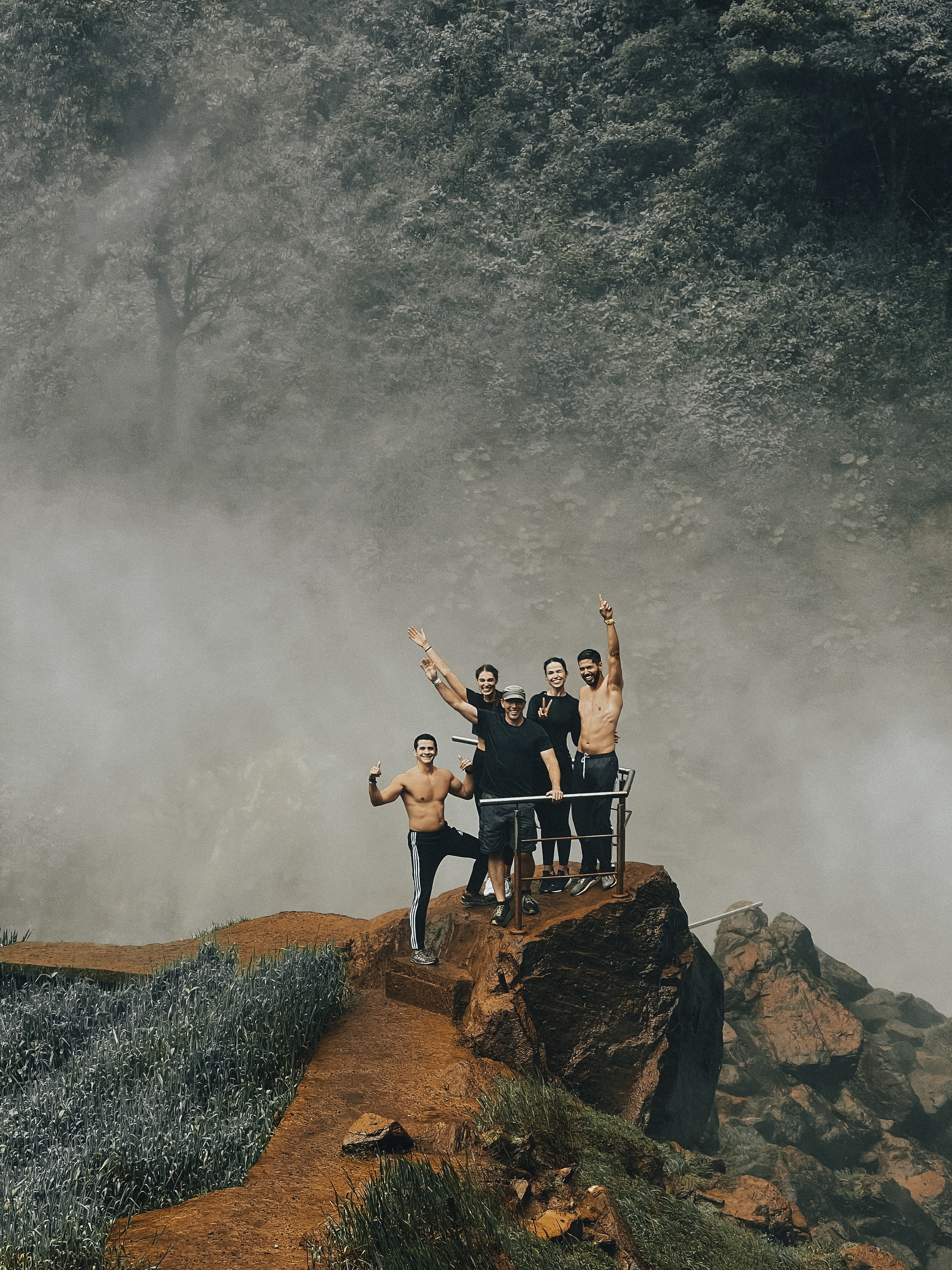 Two women and three men standing on a distant rocky mount behind a railing, surrounded in mist