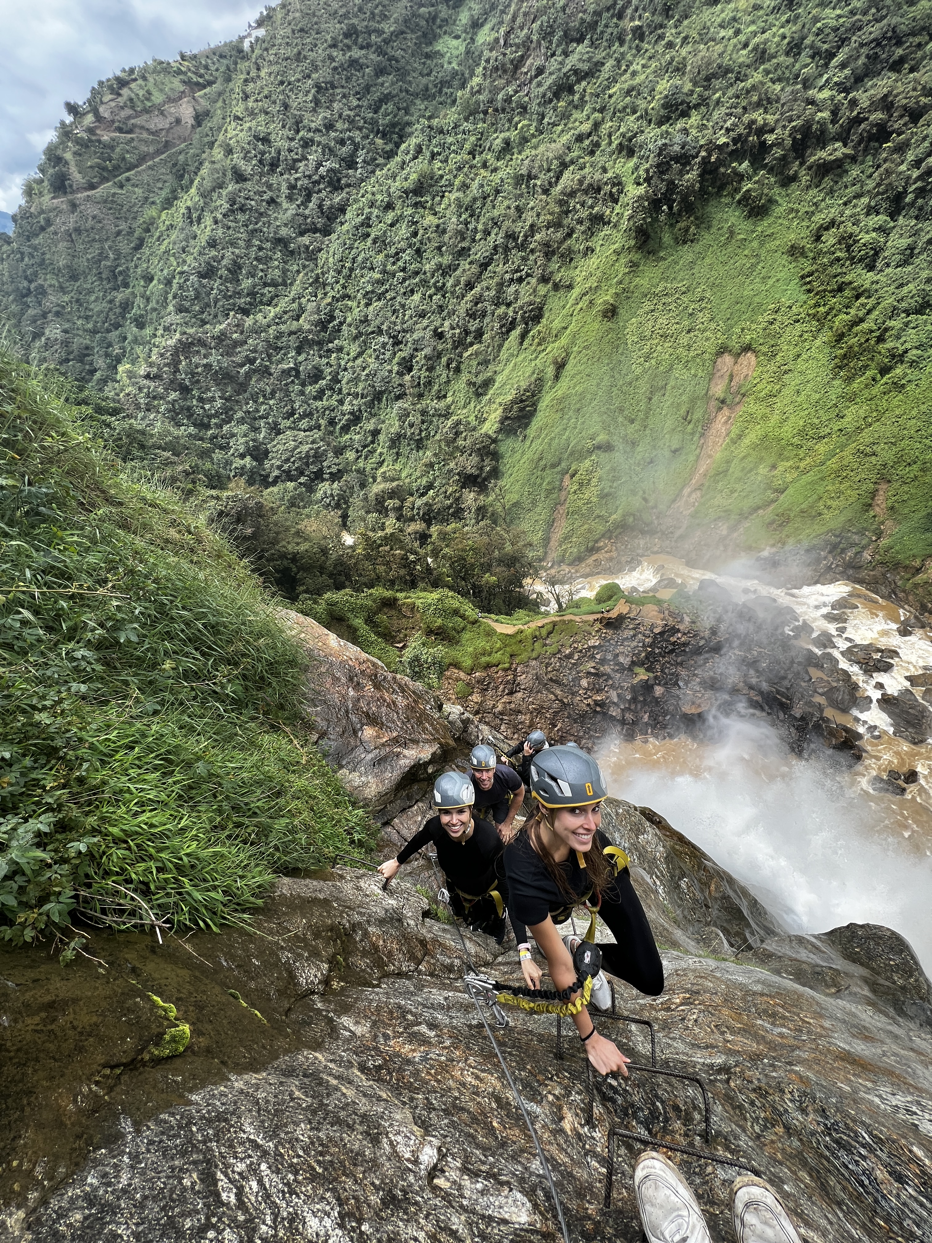 A string of tour members climbing one by one up the via ferrata with the steep valley below