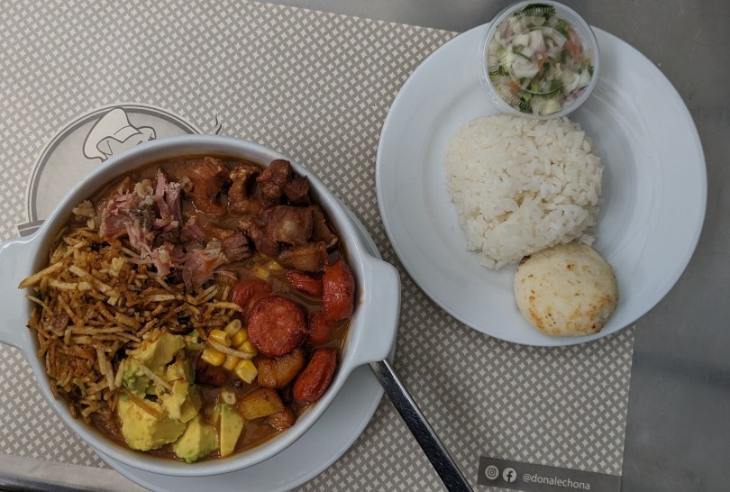 Bowl stuffed with lots of different foods with a side of rice, onion salsa, and an arepa