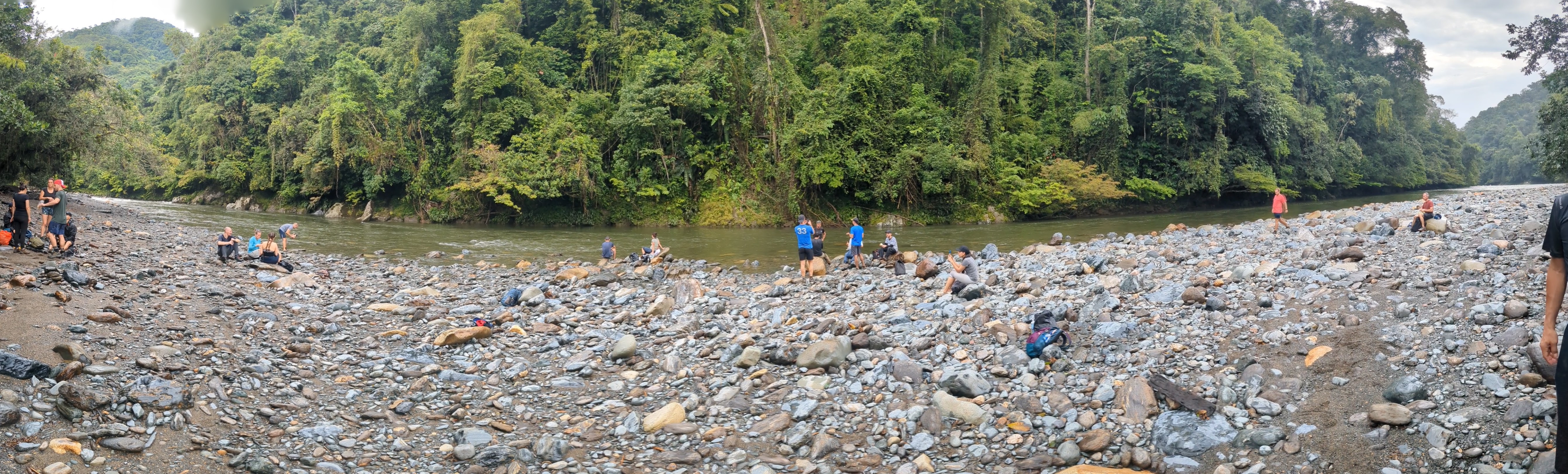 Hikers spread out along a rock beach by the river